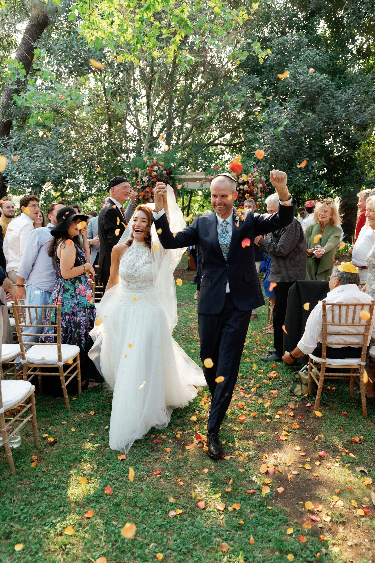 A joyful wedding celebration in a garden setting with guests throwing flower petals as the couple walks down the aisle.