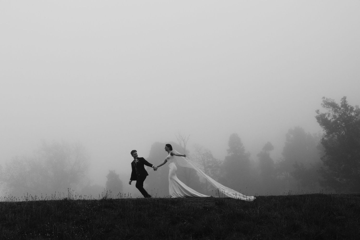 Silhouettes of two people walking along a foggy mountain road with trees in the misty background.