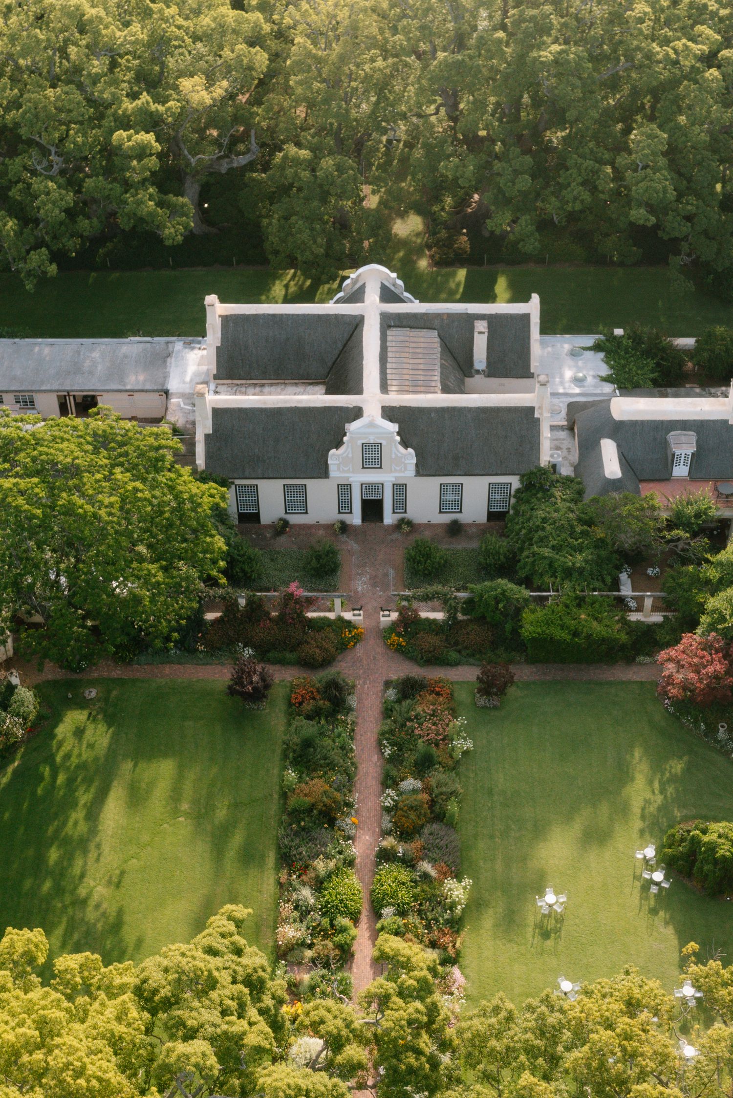 Aerial view of a Cape Dutch style manor house with symmetrical architecture and manicured gardens featuring a central pathway.