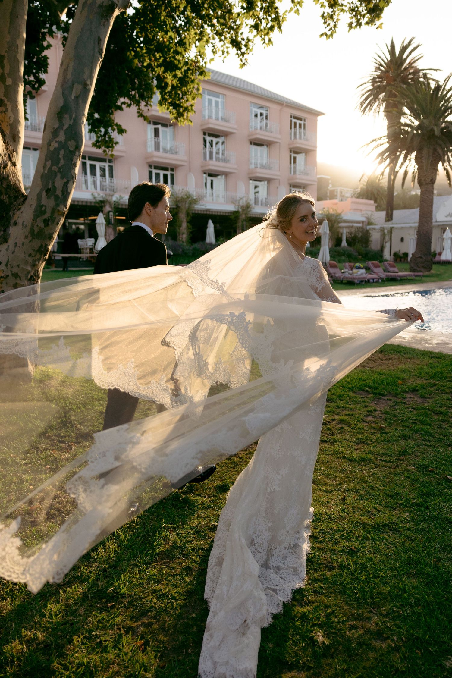 A series of sunset photos capturing a bride's veil flowing dramatically in the wind against a pink building backdrop.