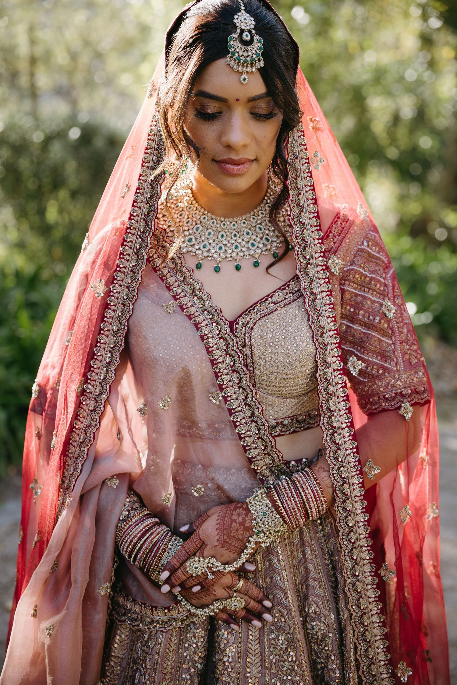 A traditional South Asian bride wearing an intricately embellished pink lehenga with detailed jewelry and embroidery.