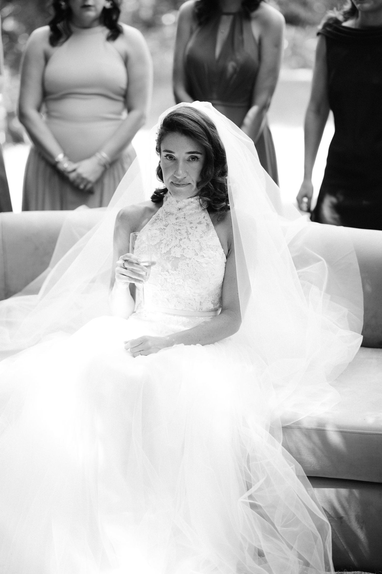 A bride in a flowing white wedding gown sits elegantly with her veil cascading around her in black and white photos.