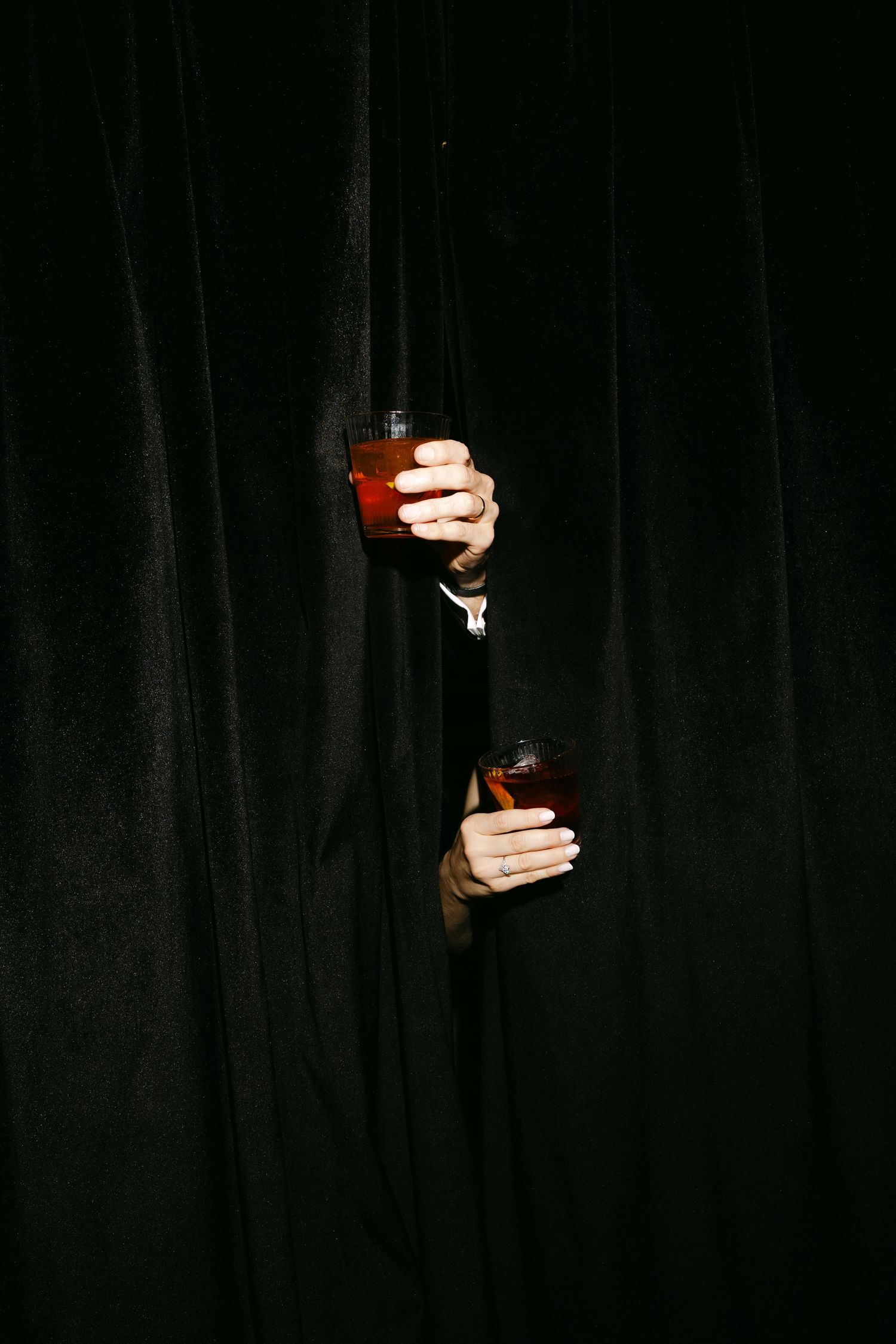 A sequence of hands emerging from darkness holding wine glasses in various positions against a black background.