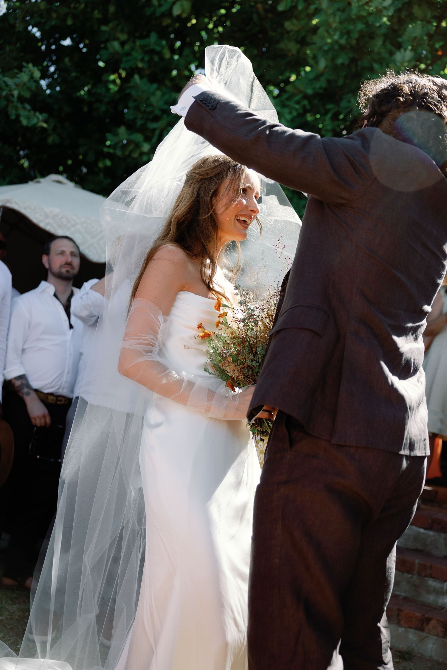 A couple shares their first dance at an outdoor wedding ceremony, with the bride wearing a flowing white dress and veil.