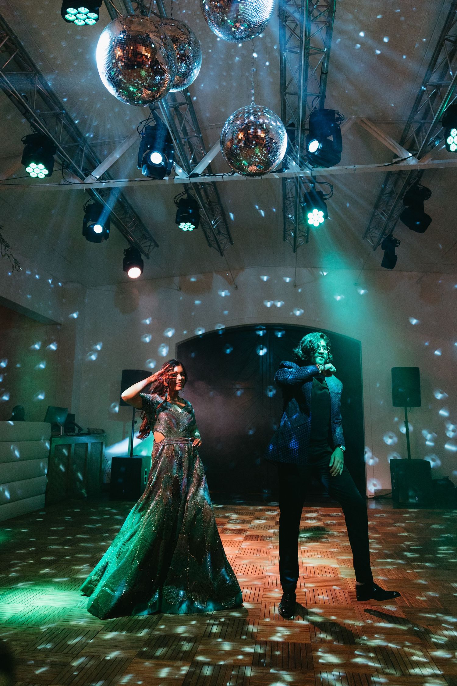 A couple dancing under disco balls and colorful lights at an indoor party with green lighting effects.