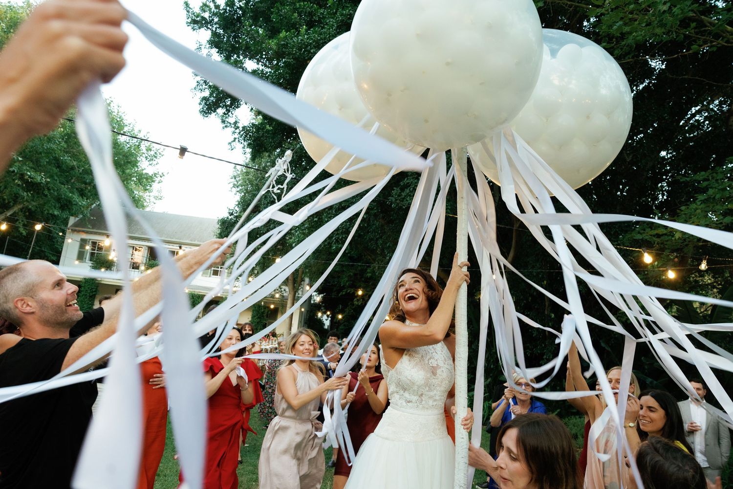 Bride celebrates outdoors with white balloon streamers at a festive wedding reception.
