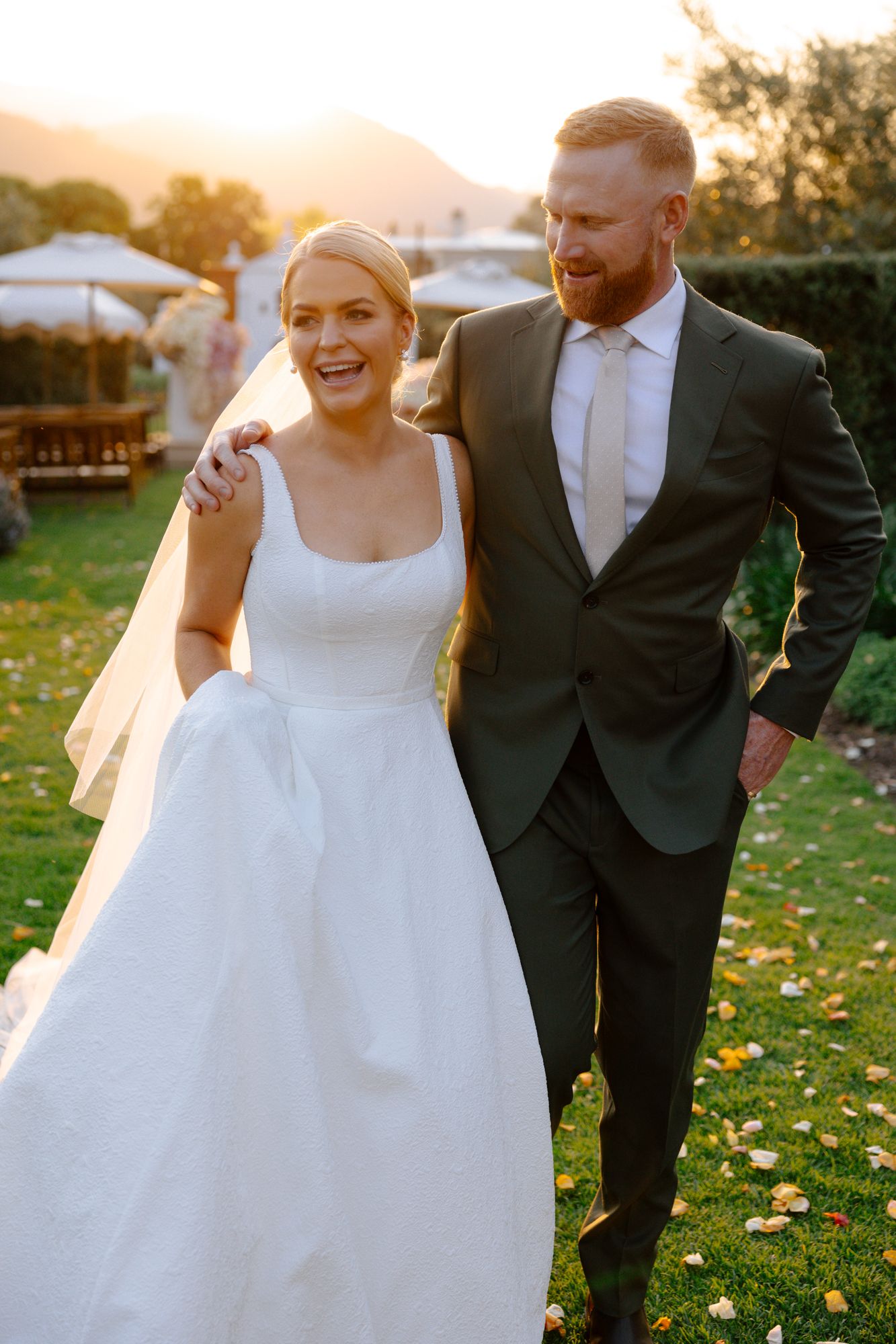 A joyful wedding couple shares candid moments together at sunset in a field with scattered yellow flowers.