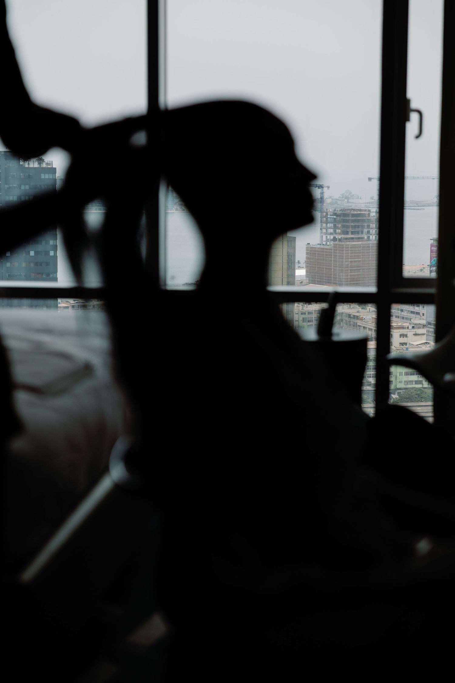 Silhouette of a person styling their hair against a window with an urban cityscape in the background.