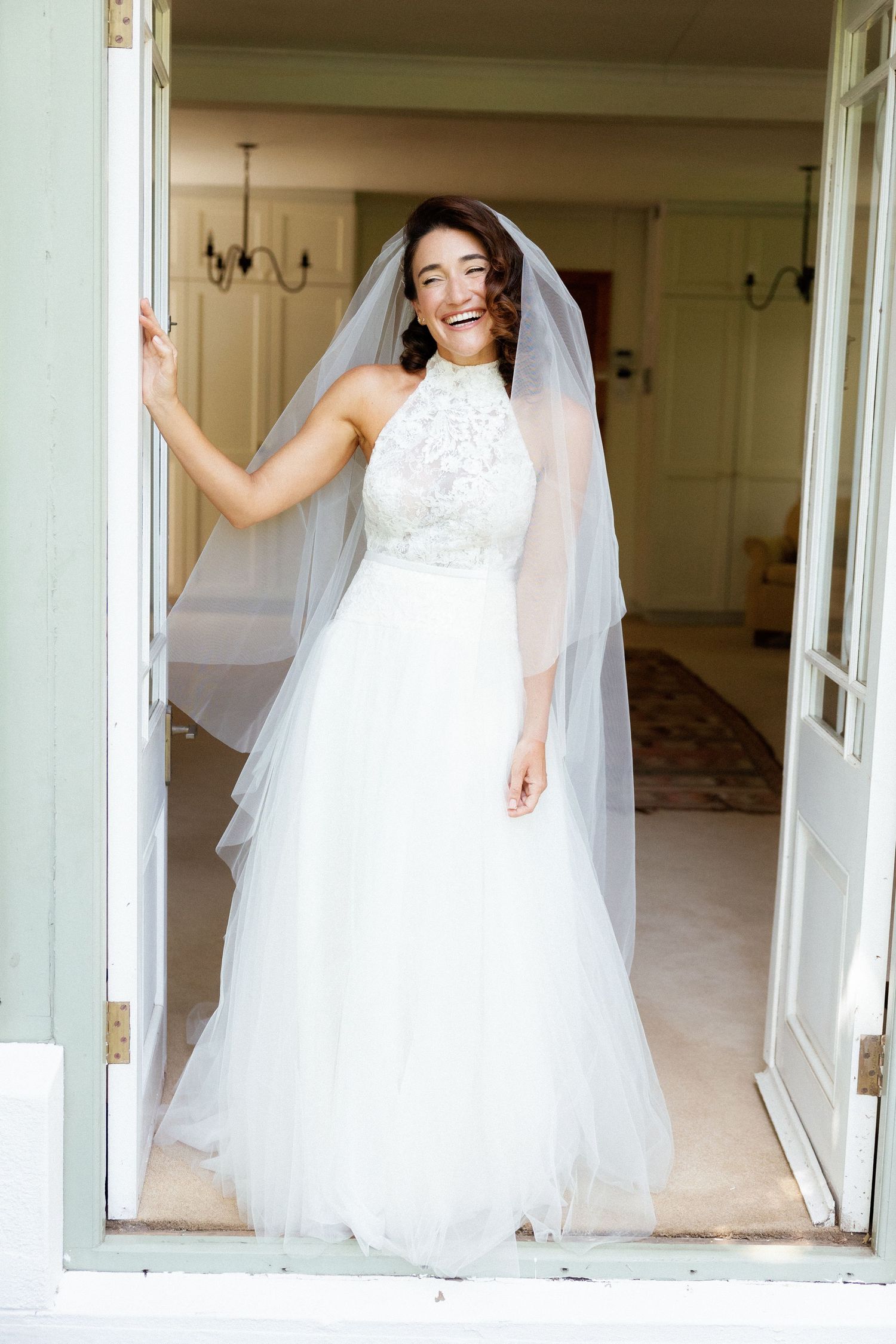 A bride in a flowing white wedding gown and veil poses in a series of candid shots in a light-filled room.