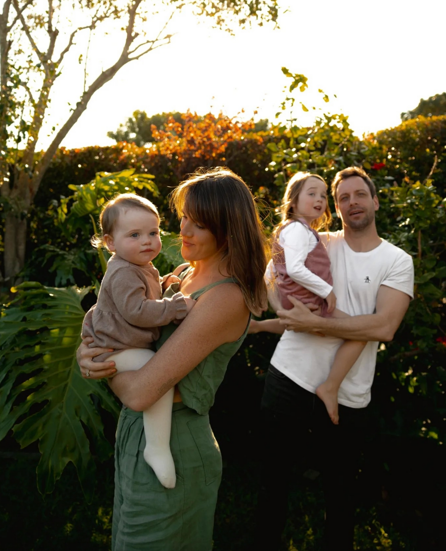 A family poses together in a garden with tropical plants during sunset.