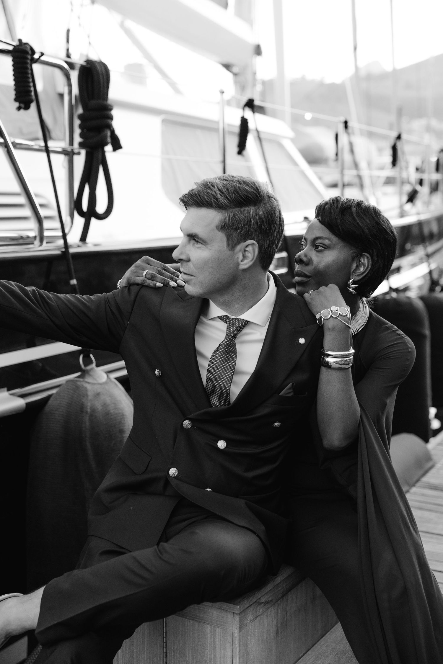 Elegant interracial couple posing on a luxury yacht deck in formal attire, black and white photography.