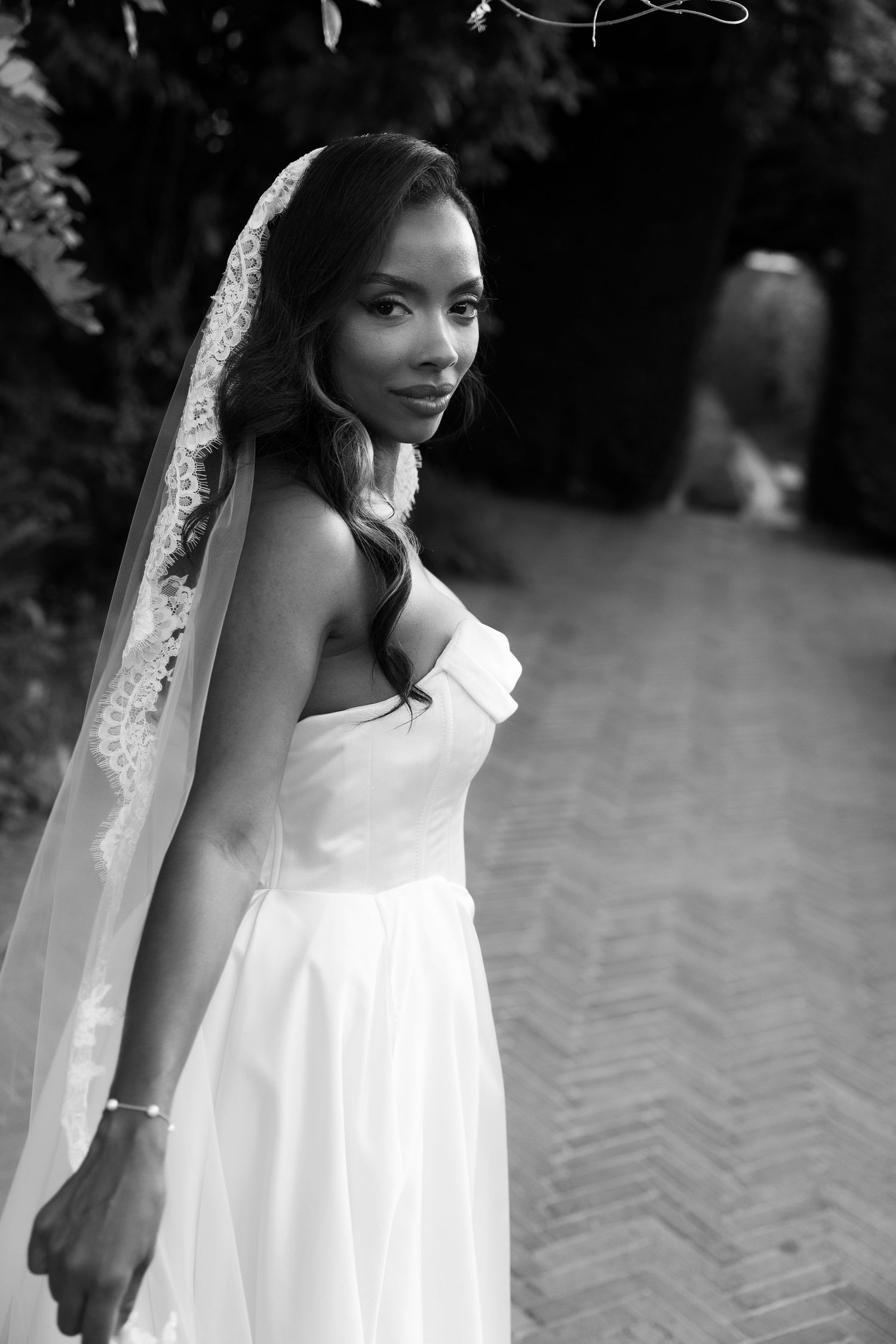 Elegant black and white portrait of a bride in a strapless wedding gown and delicate lace veil in an outdoor setting.