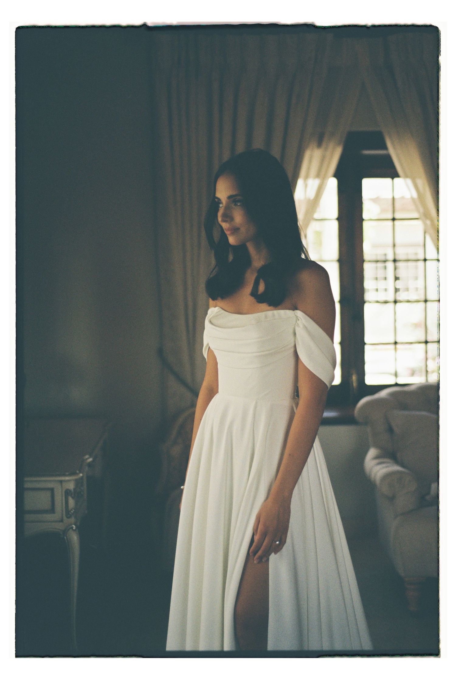 A flowing white off-shoulder wedding dress photographed in vintage style lighting.