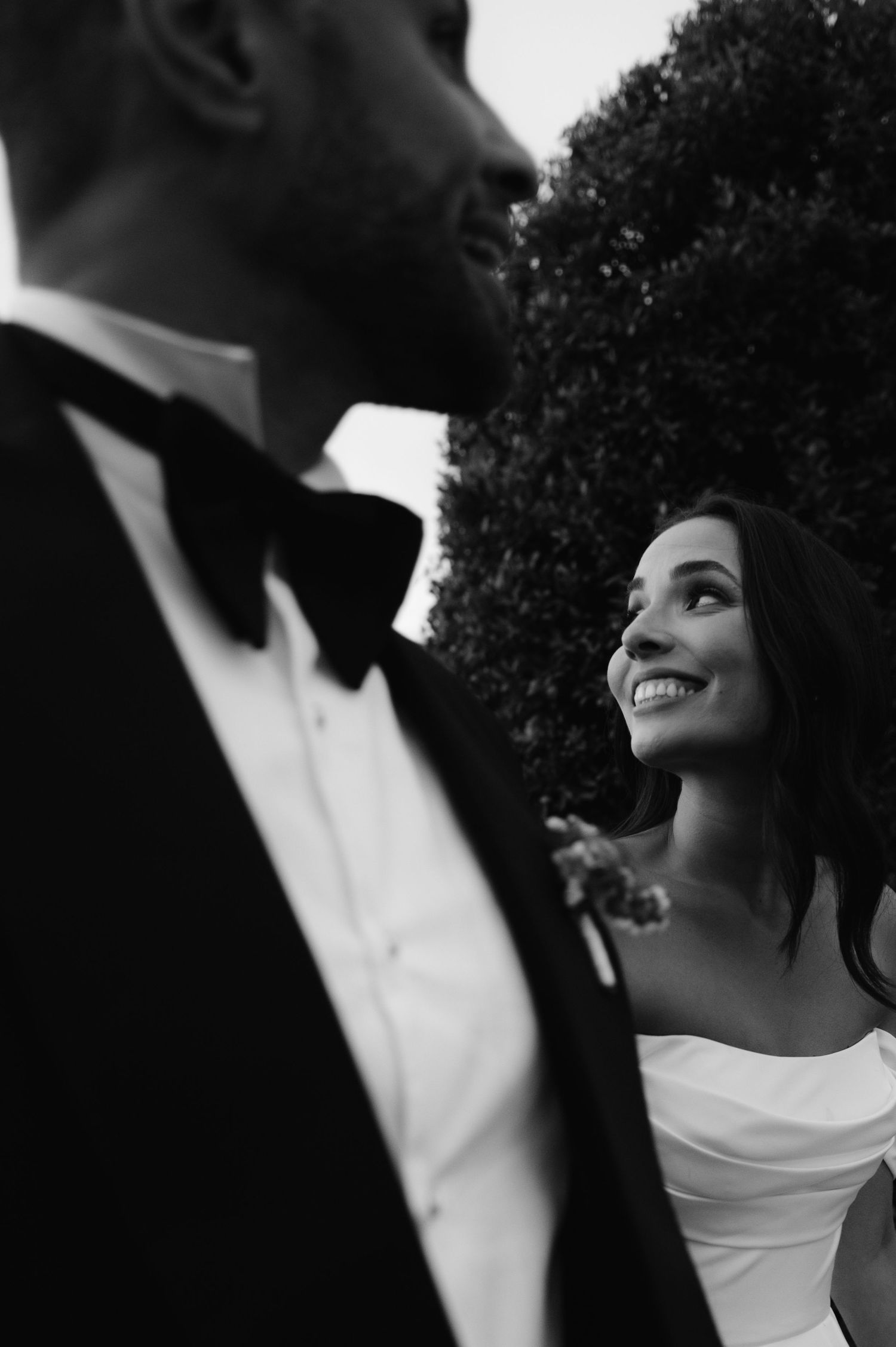 A romantic black and white wedding photo showing a couple in formal attire sharing an intimate moment outdoors.