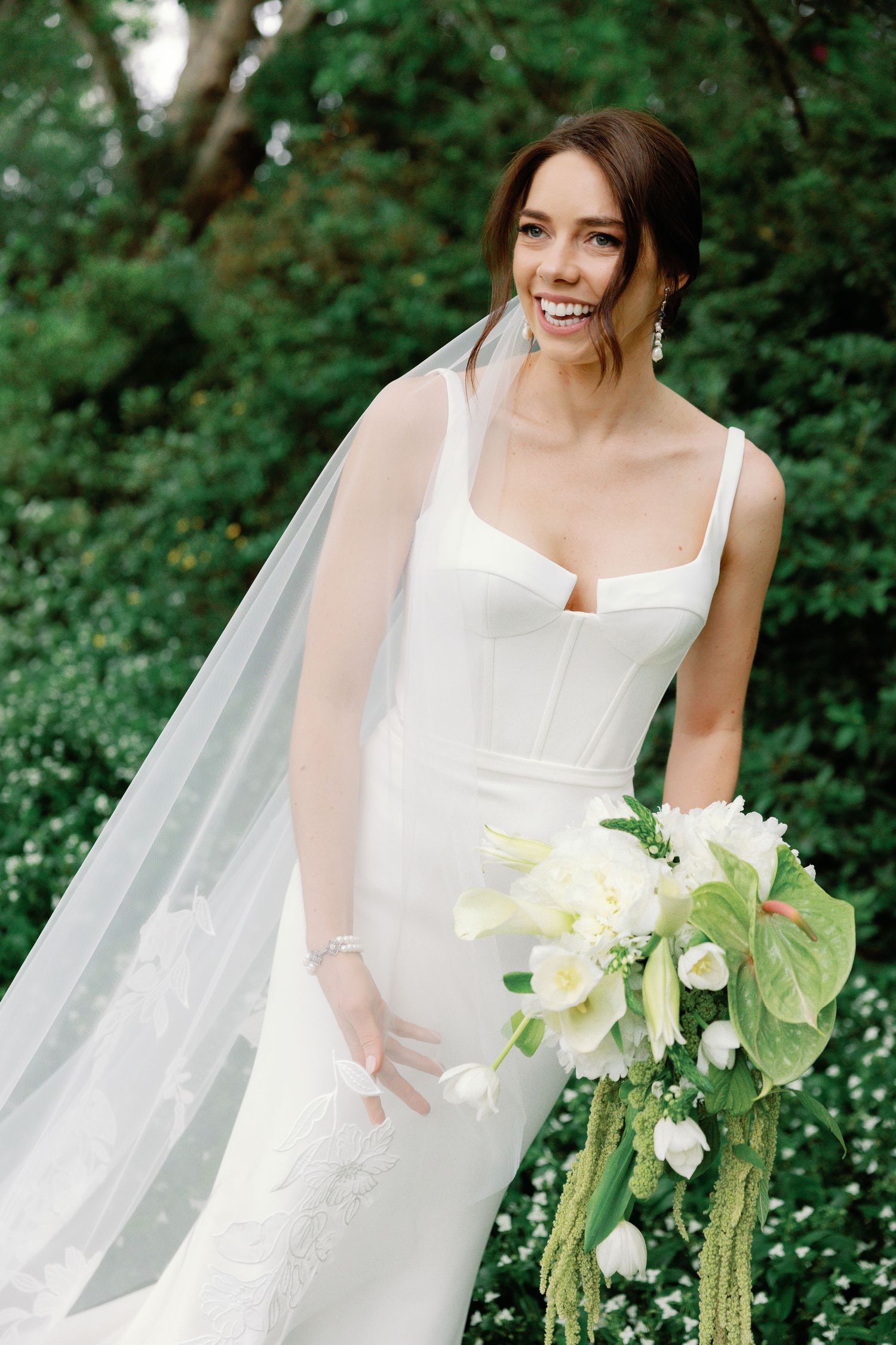 Elegant bridal portrait with flowing veil and white bouquet in a garden setting.