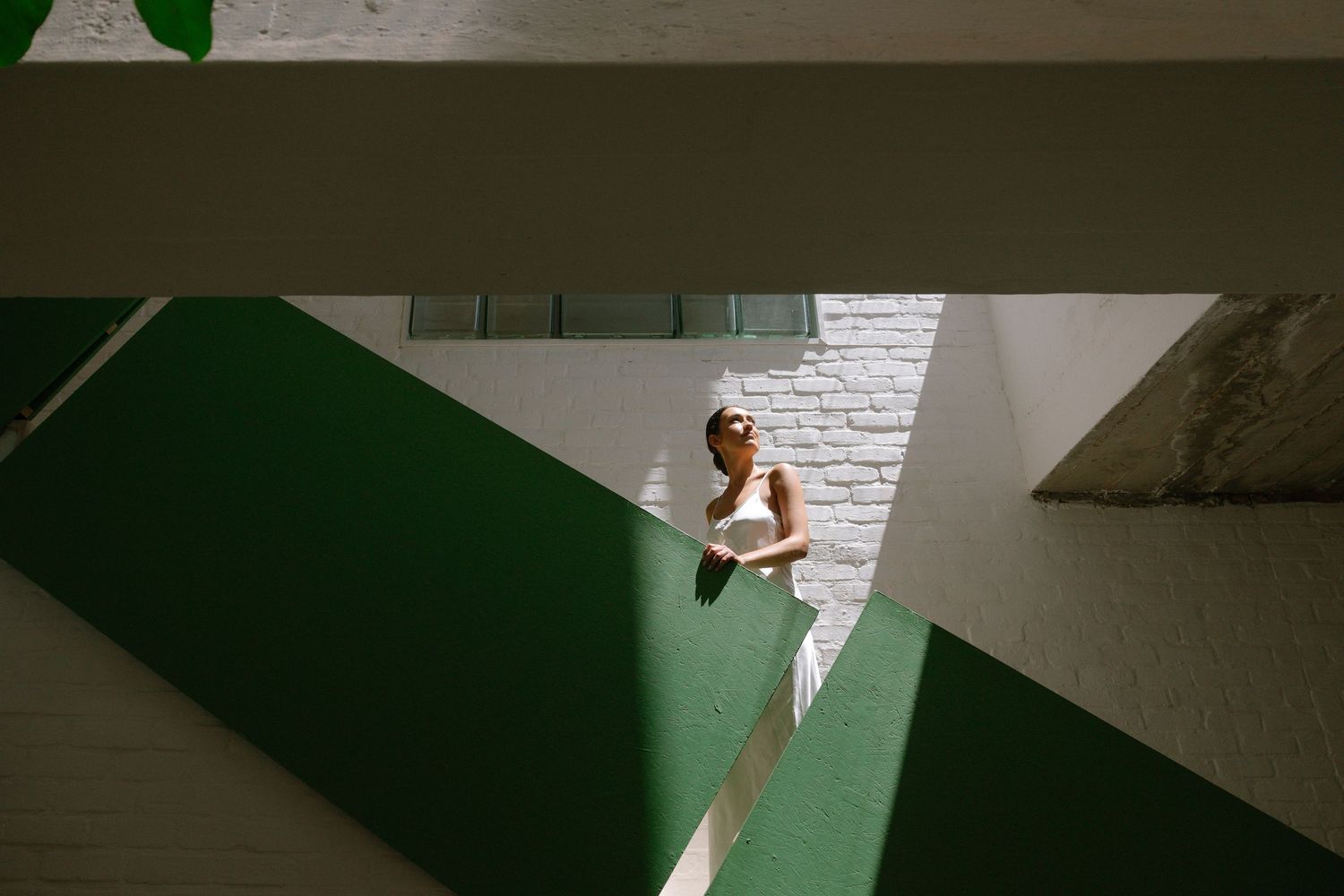 A person in white clothing sits on a green geometric staircase illuminated by dramatic angular lighting.