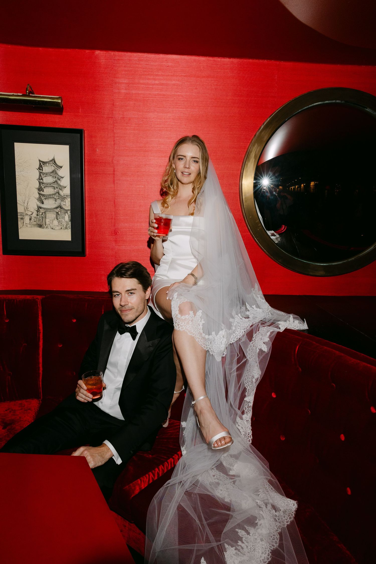 Wedding celebration photos with red walls showing guests and a bride in a white dress relaxing on dark furniture.