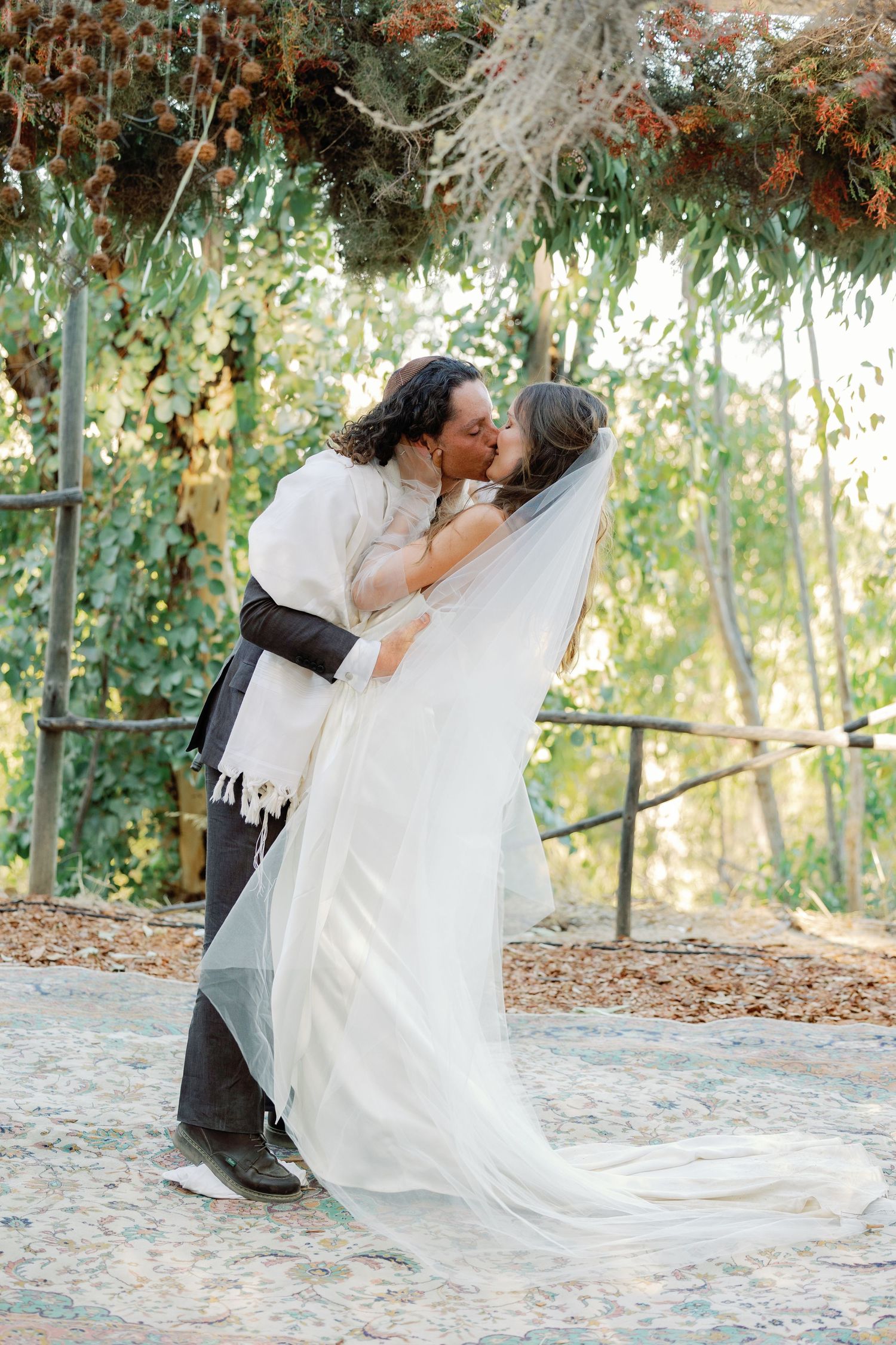 A romantic wedding moment captured outdoors with flowing white dress and veil against a natural garden backdrop.