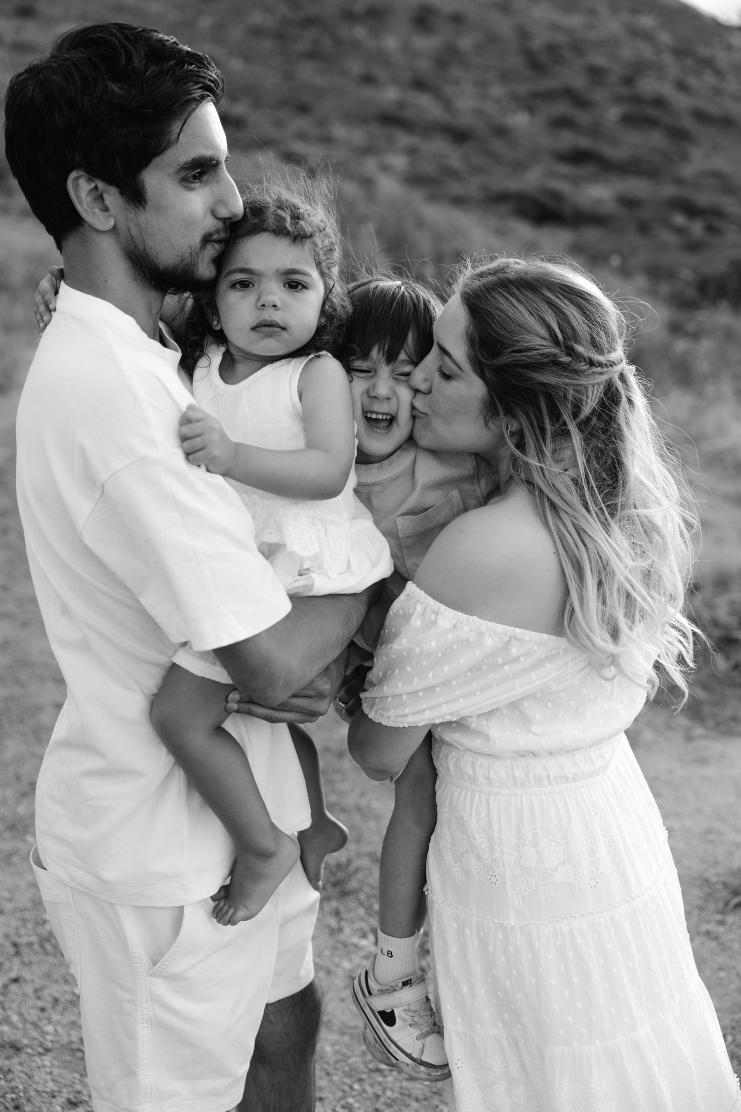 Family of four in white outfits poses together against a mountainous backdrop.