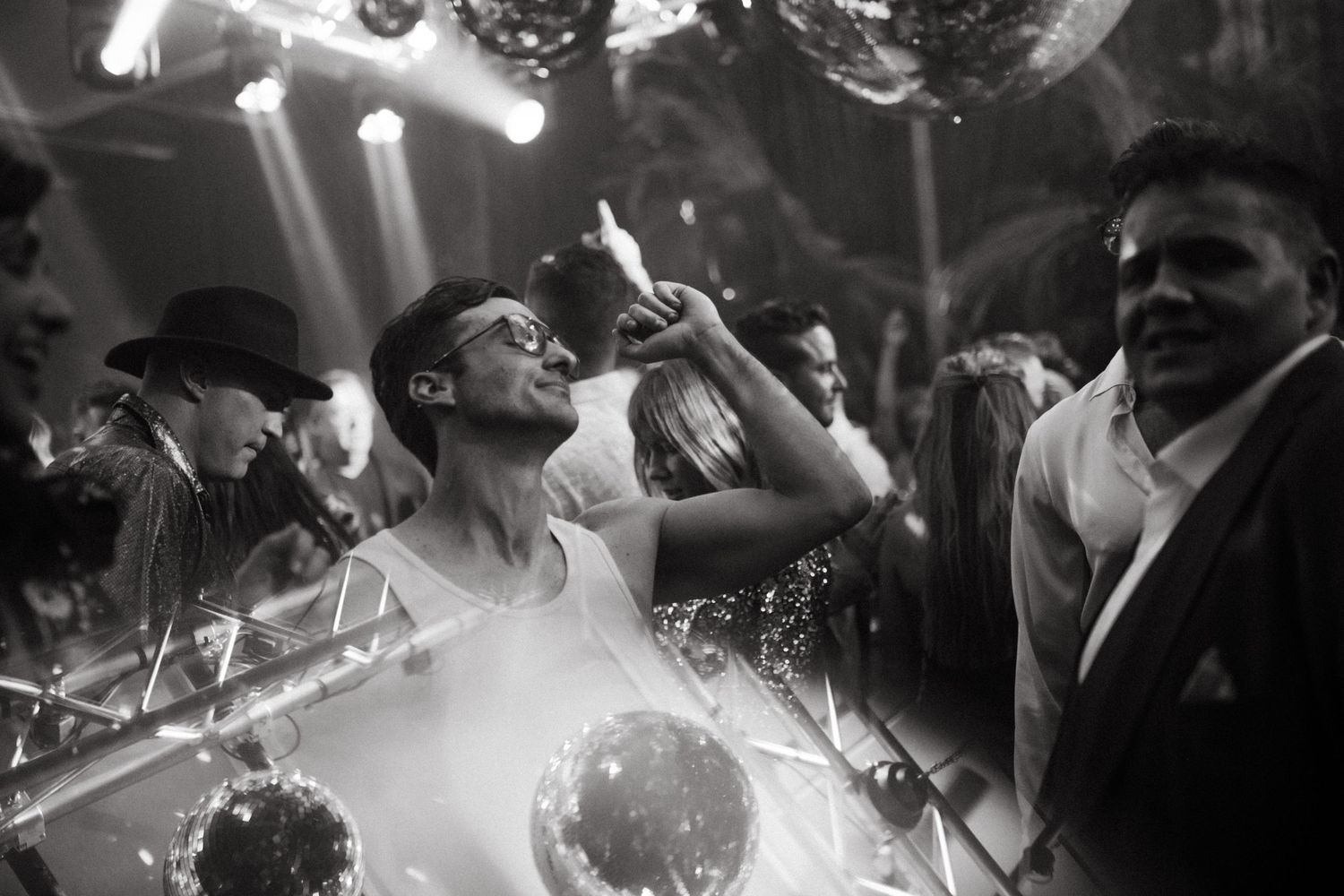 Black and white photo of people dancing at a nightclub with disco balls and stage lights.