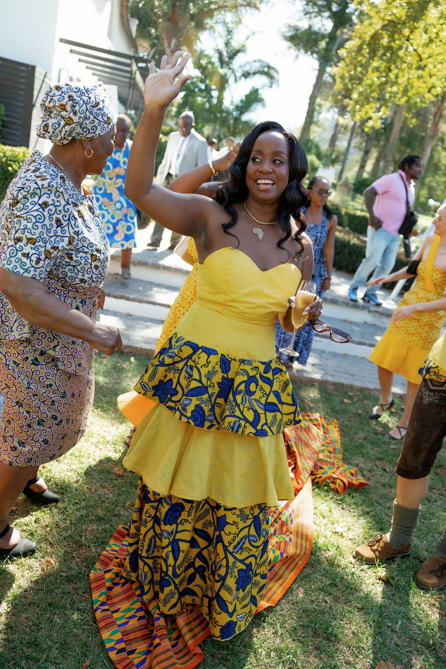 Woman in vibrant yellow and African print dress dancing outdoors at a cultural celebration.