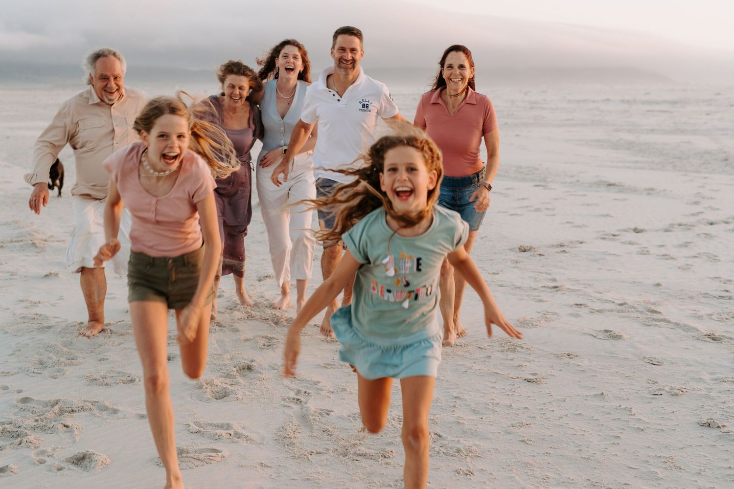People running and laughing together on a beach during sunset.
