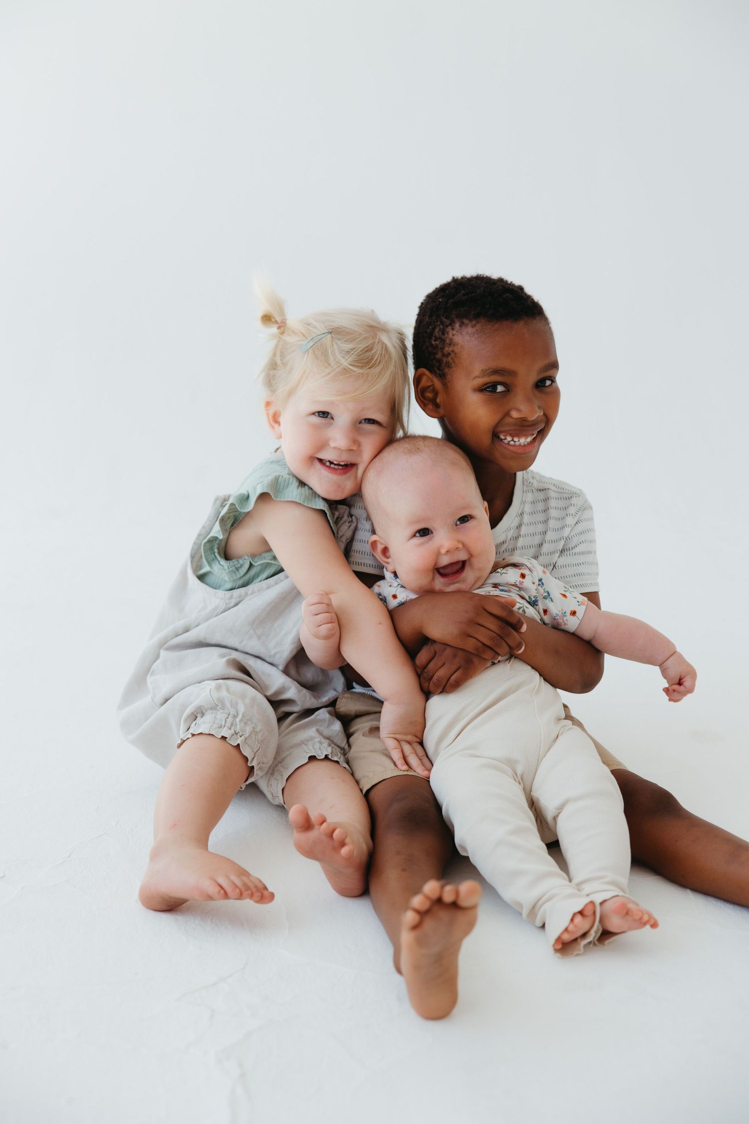 Three children sitting together on white background sharing joyful smiles.