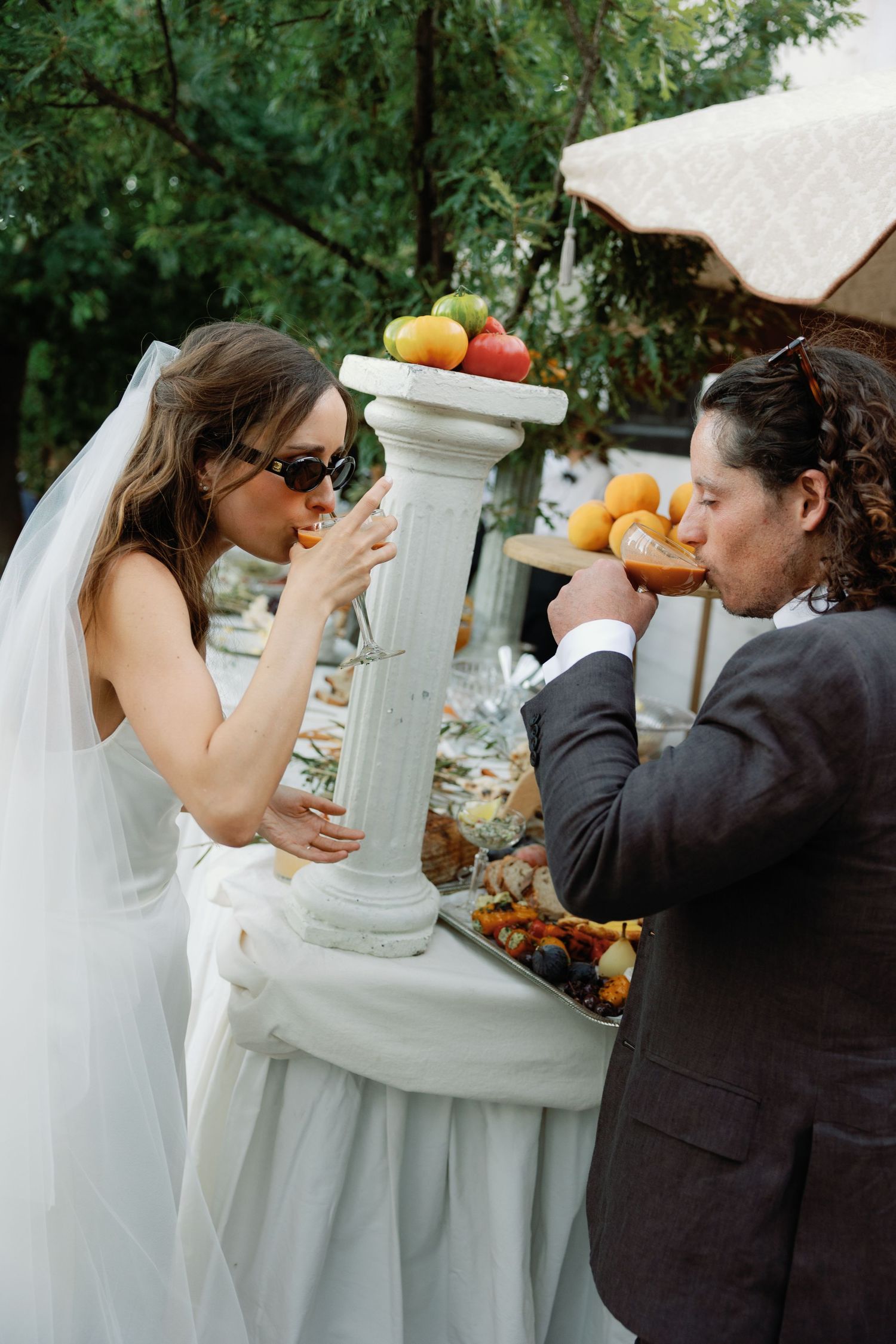A bride and groom share a playful moment feeding each other during their wedding reception outdoors.
