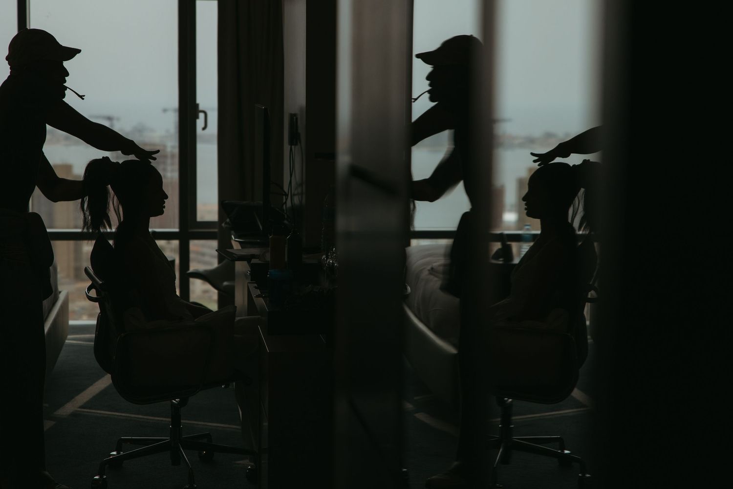 Silhouette of a hairstylist working on a client in a salon, reflected in glass with moody dark tones.