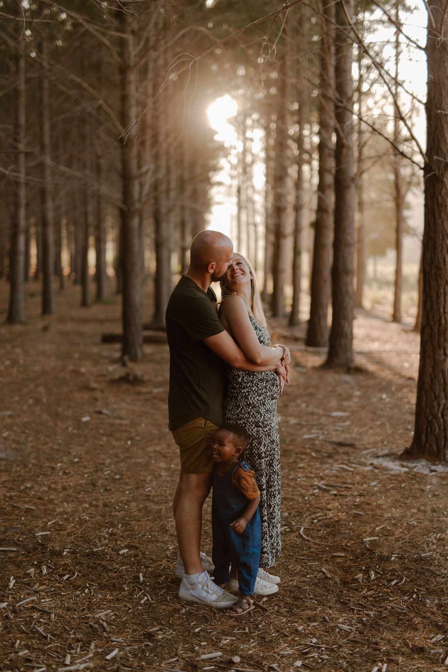 A tender family moment captured in a pine forest with sunlight streaming through the trees.
