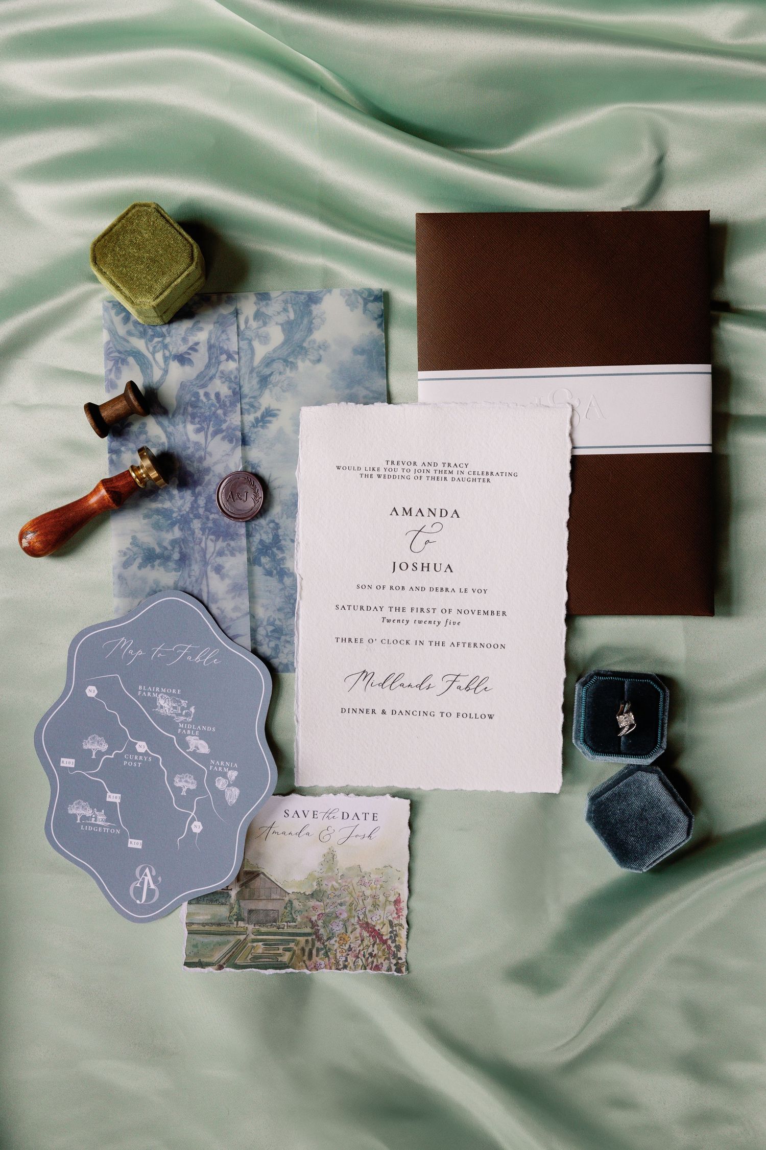 Elegant wedding invitation suite with blue floral details laid out on mint green silk fabric.