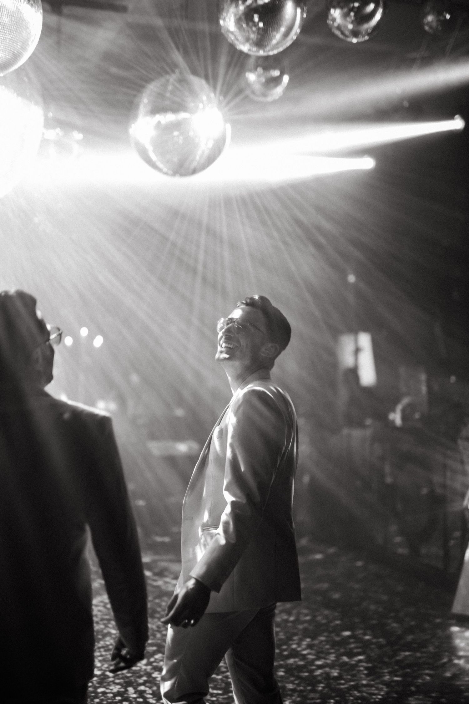 Black and white photo of a man smiling under disco ball lights at a nightclub event.