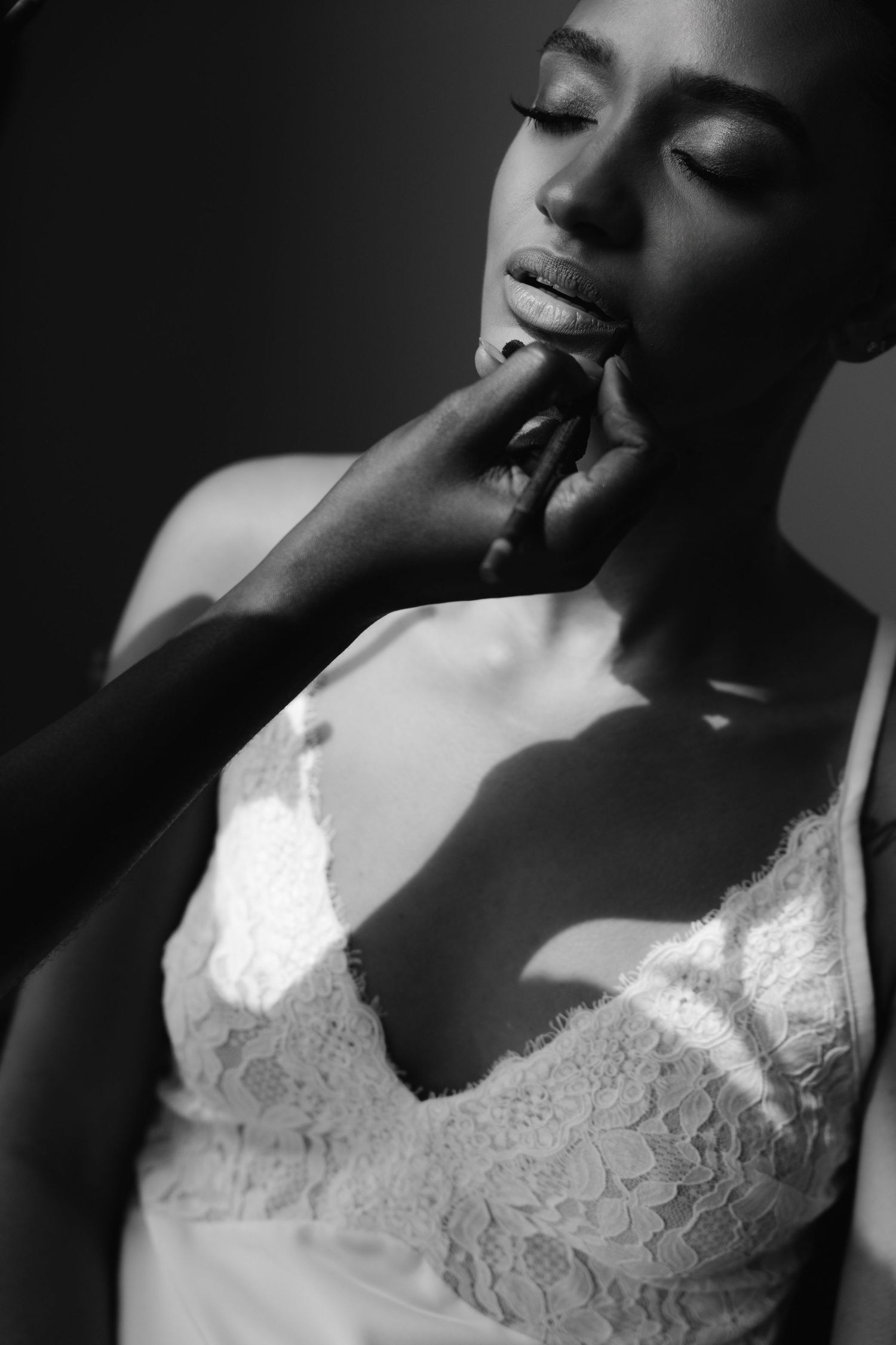 Black and white portrait of a woman in lace bridal gown with eyes closed, hand gently touching her chin.