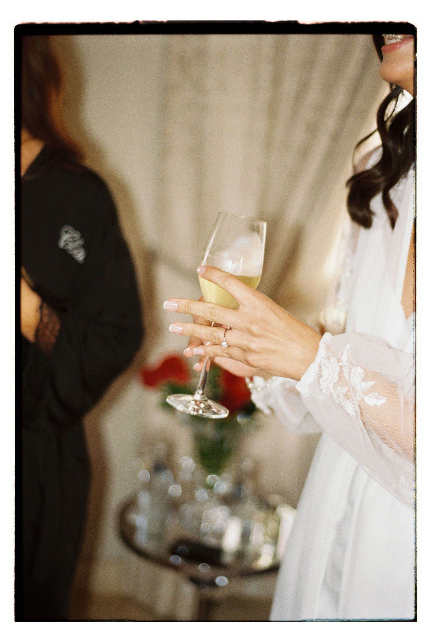 A delicate hand holding a champagne glass with an engagement ring visible.