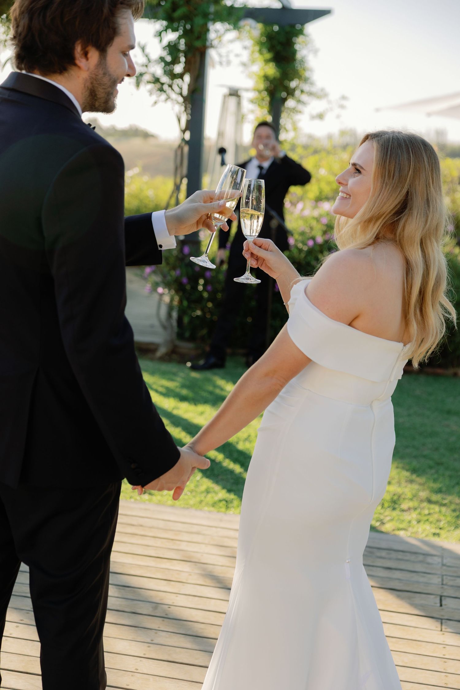 Bride and groom toasting with champagne glasses outdoors at their wedding reception in elegant formal attire.