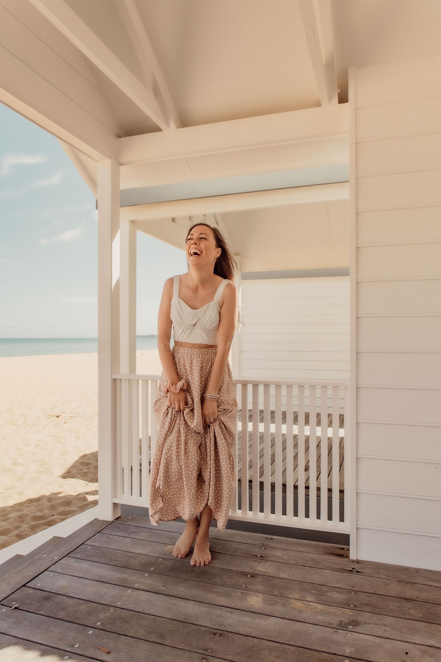 Woman in summer dress laughing on white beach house porch with ocean view.