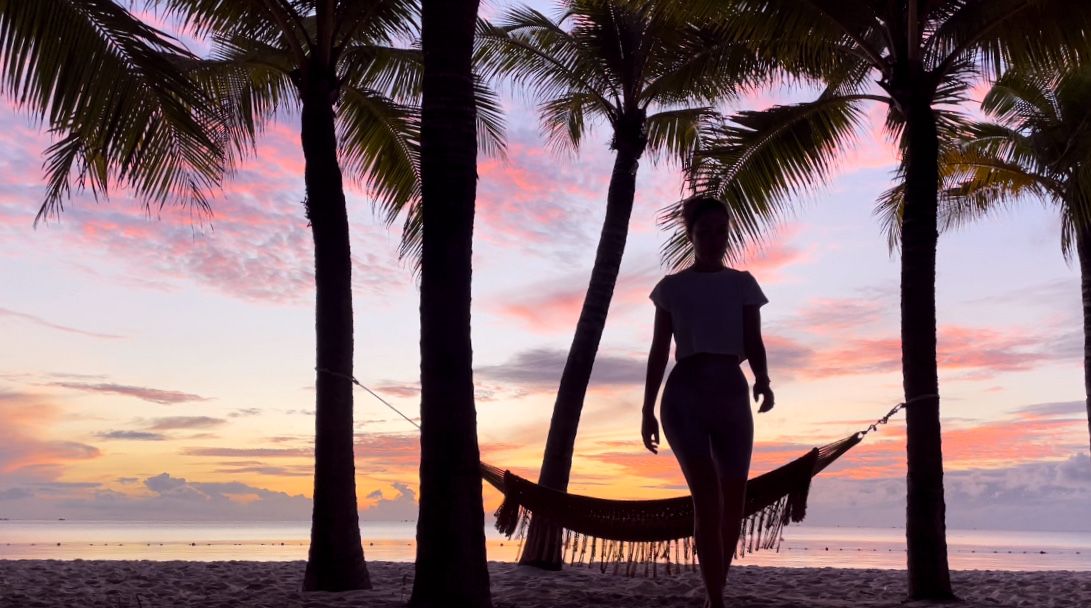 Silhouette of palm trees frame a hammock scene during a vibrant beach sunset.