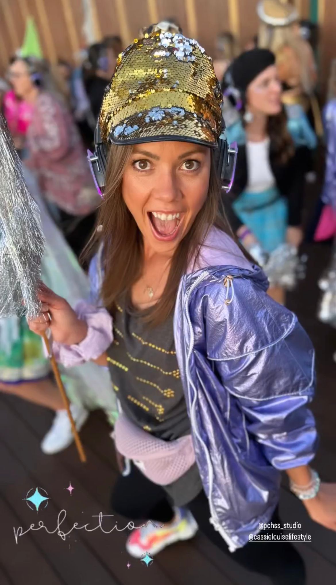 Partygoer in sparkly gold cap and purple jacket poses energetically at a festive event.