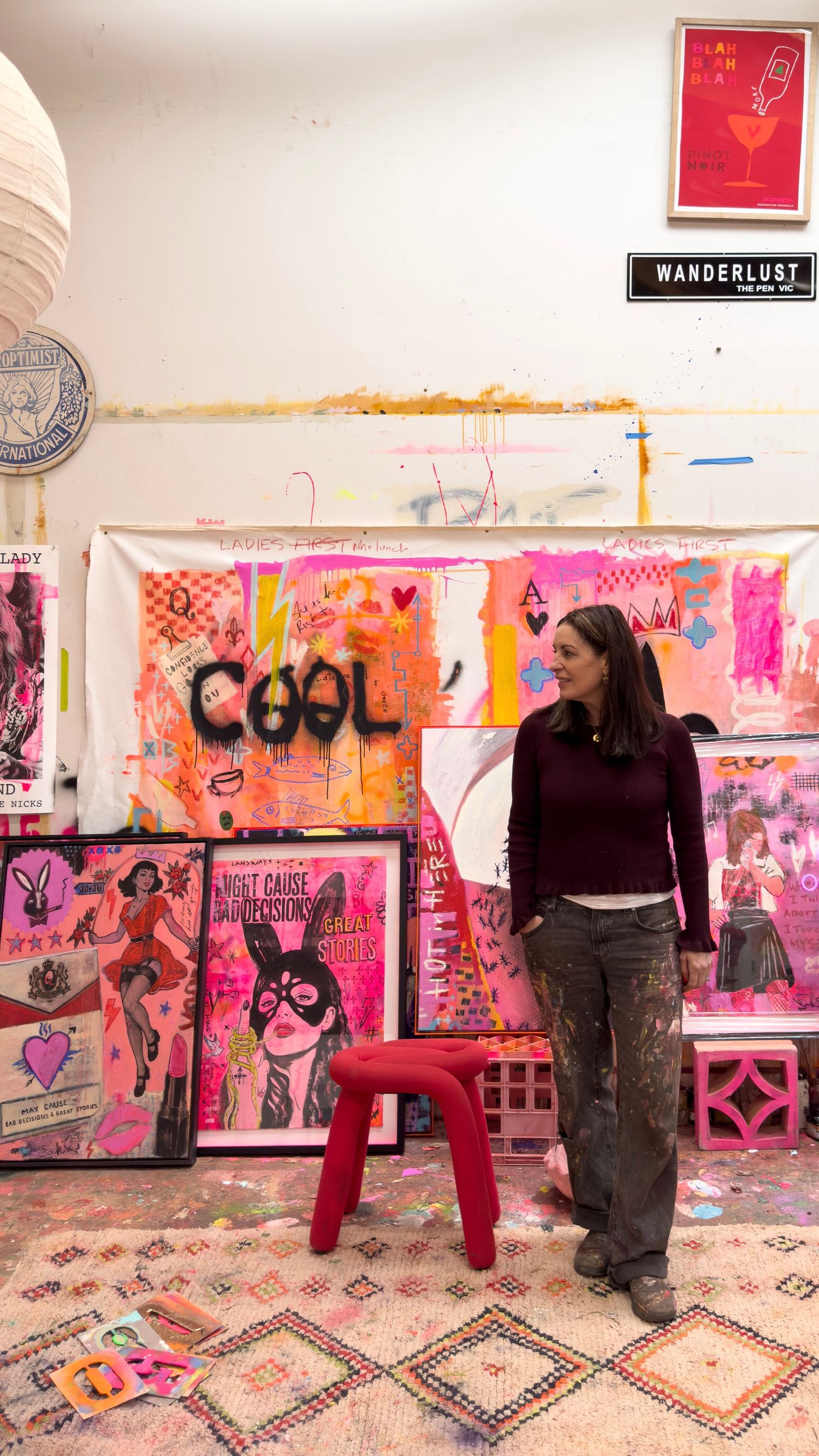 Artist stands in colorful pink art studio surrounded by bold pop art paintings with COOL graffiti text.
