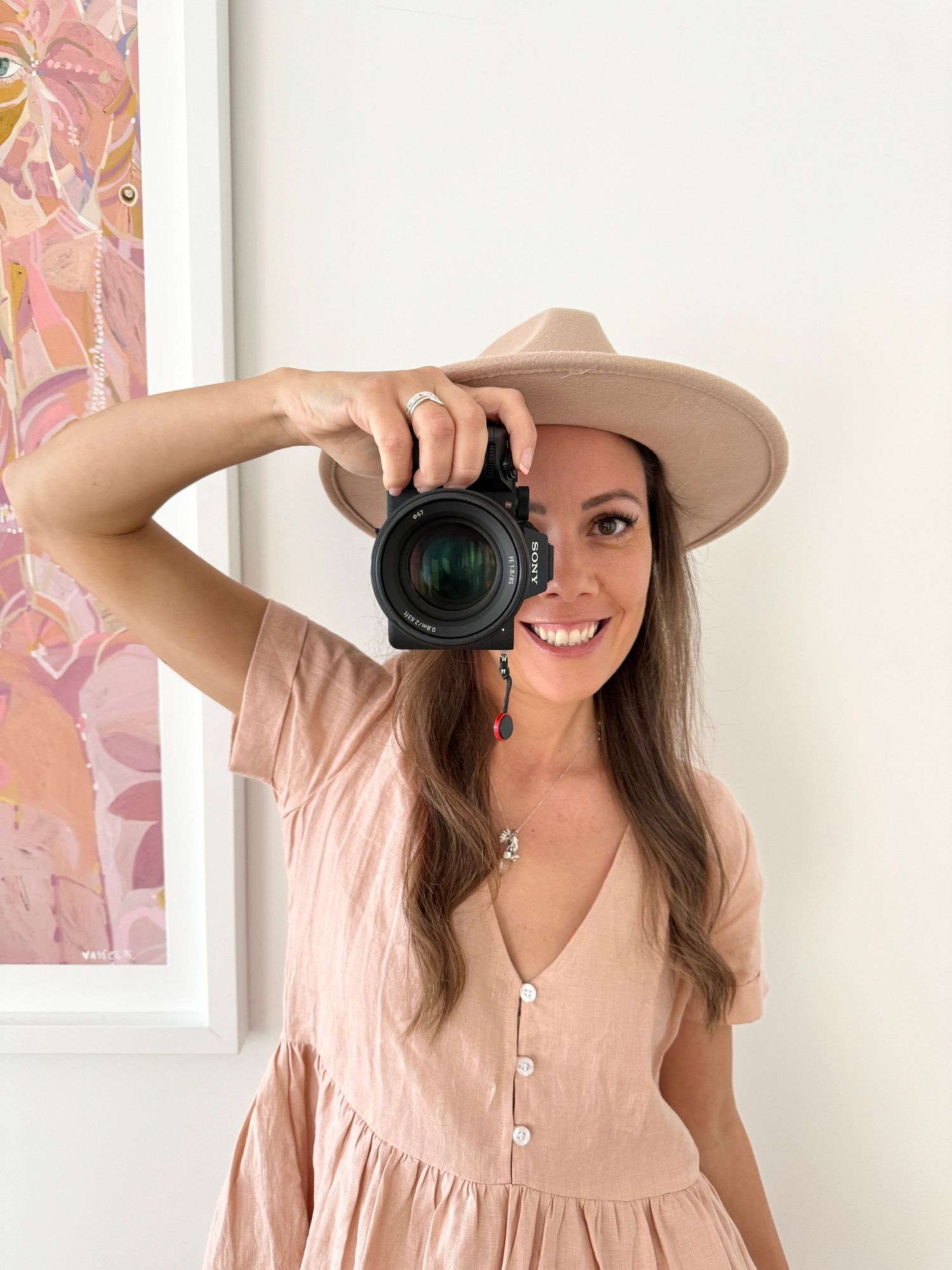 Lifestyle photography scene with camera and pink floral wall art background.