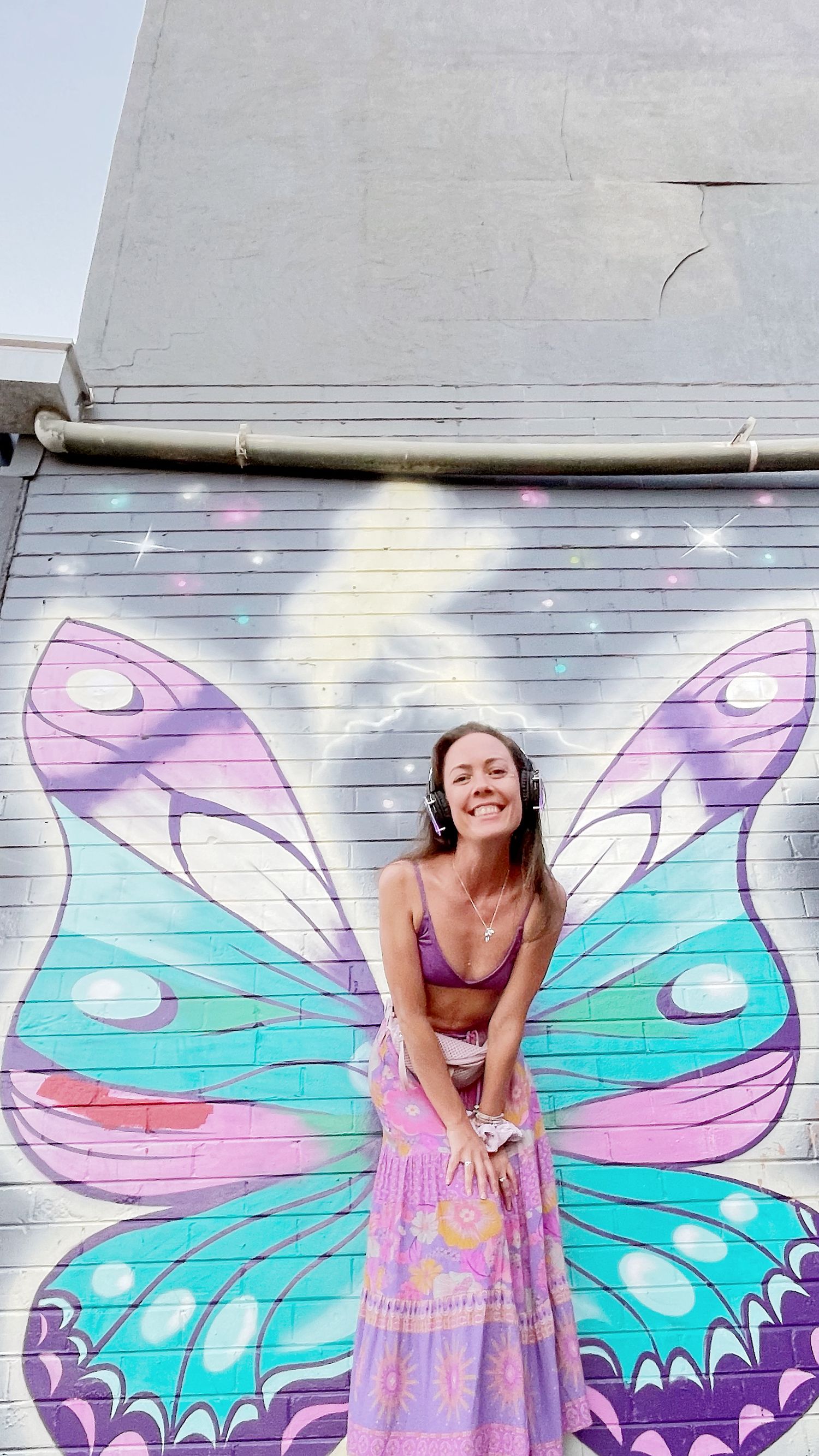 Vibrant butterfly wing street art mural in turquoise and purple creates photo opportunity.