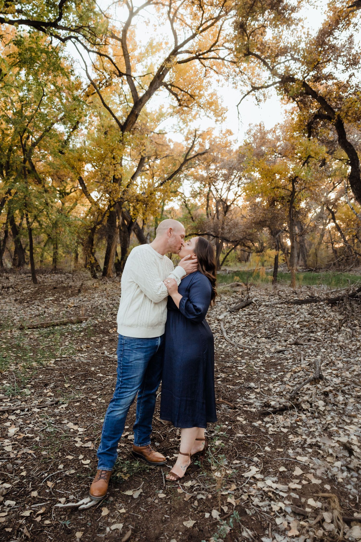 Couple sharing a romantic kiss in an autumn forest, surrounded by golden foliage and fallen leaves.
