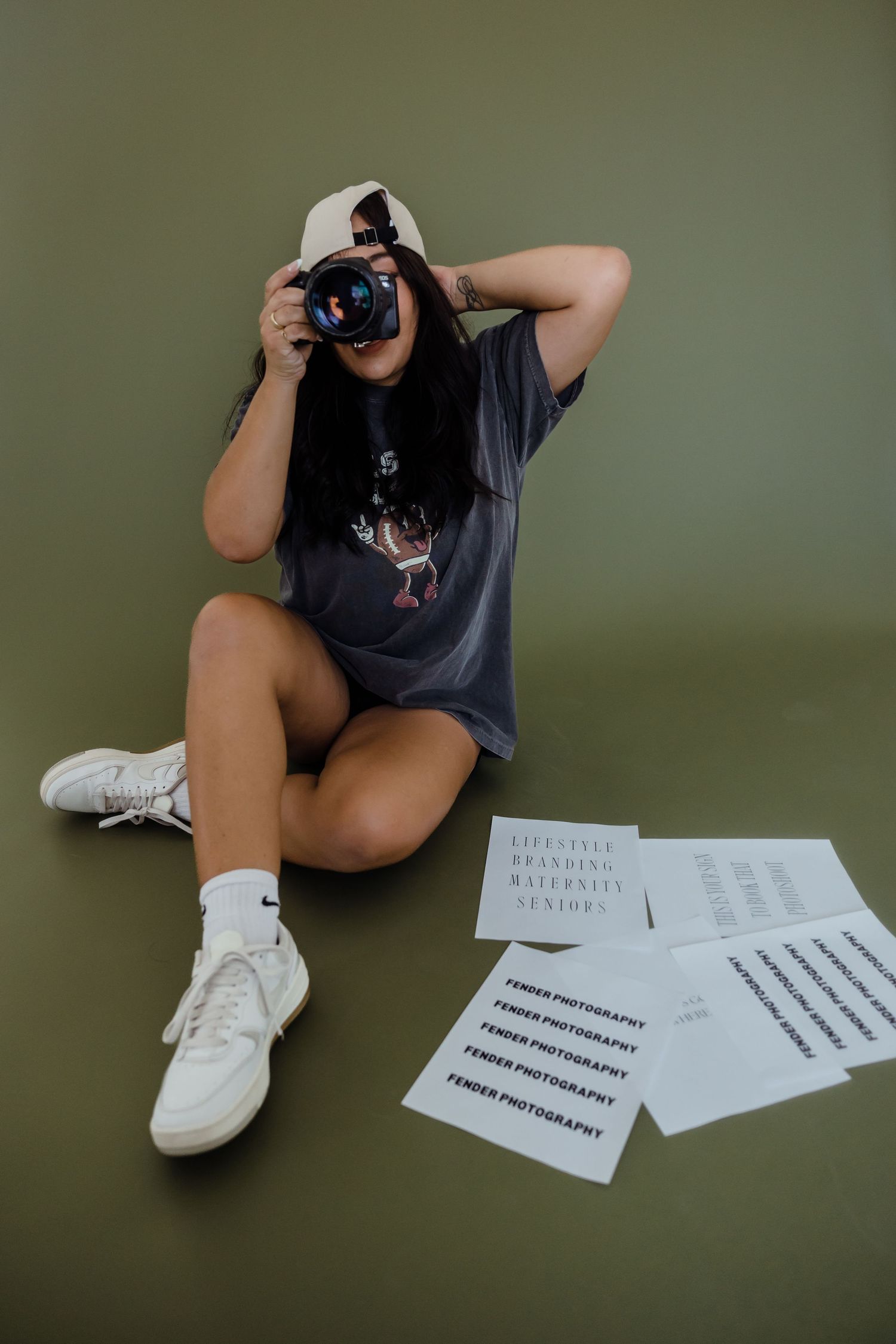 Photographer sitting on green floor with camera, surrounded by Fender Photography branded papers.