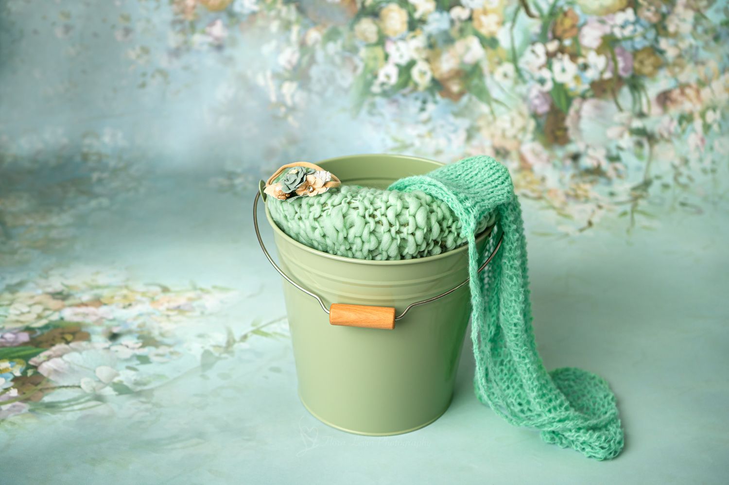 sage green metal bucket with knitted mint green wrap  on floral background for newborn photography prop.