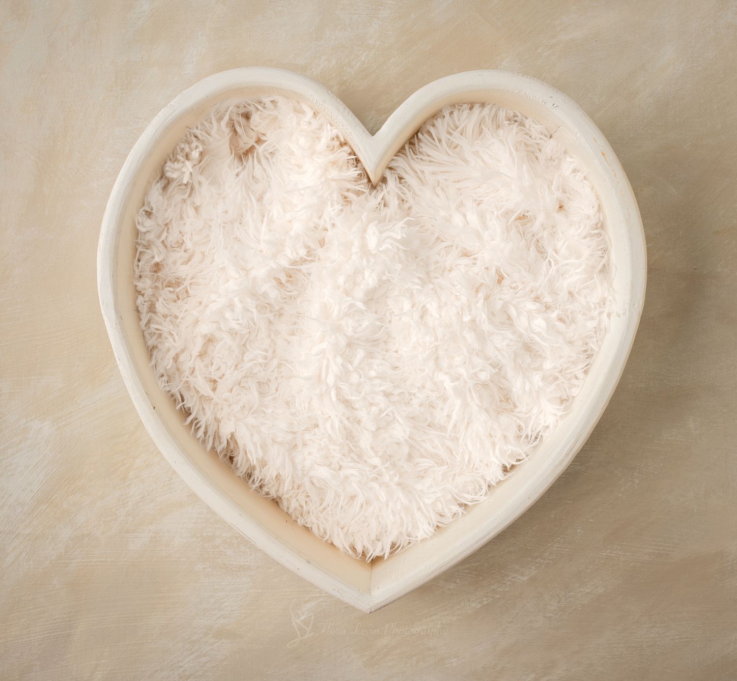 White heart-shaped bowl filled with soft fluffy white faux fur fabric, perfect for newborn photography props.
