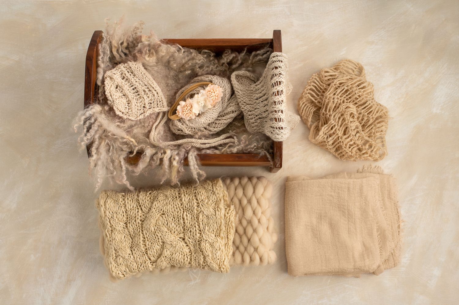 Newborn photography props including a wooden crate, knit wraps, lace bonnet, and neutral textured blankets in beige tones.