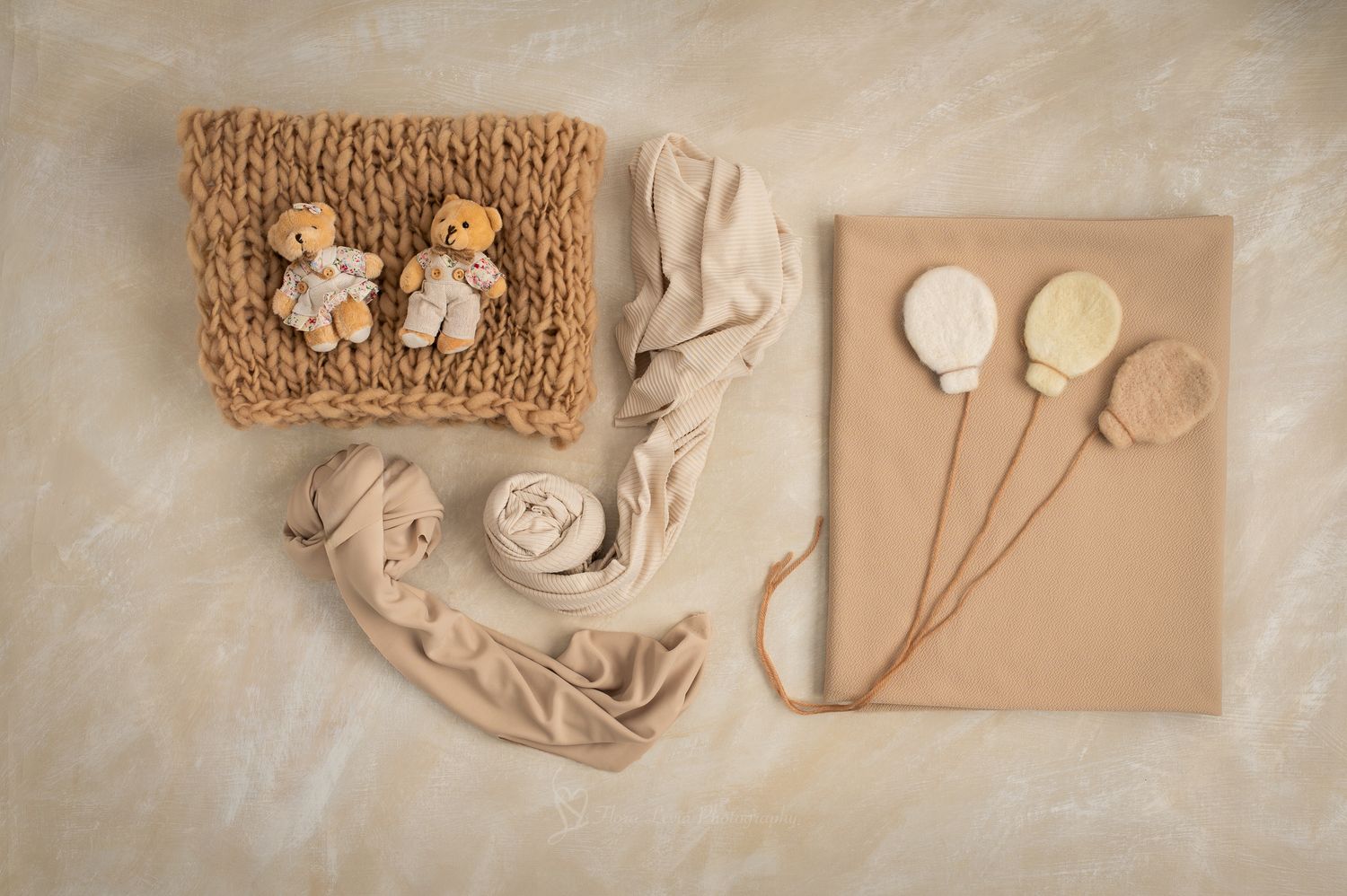 Neutral beige newborn photography props including knit blanket, teddy bears, yarn, fabric wrap, and balloon decorations.