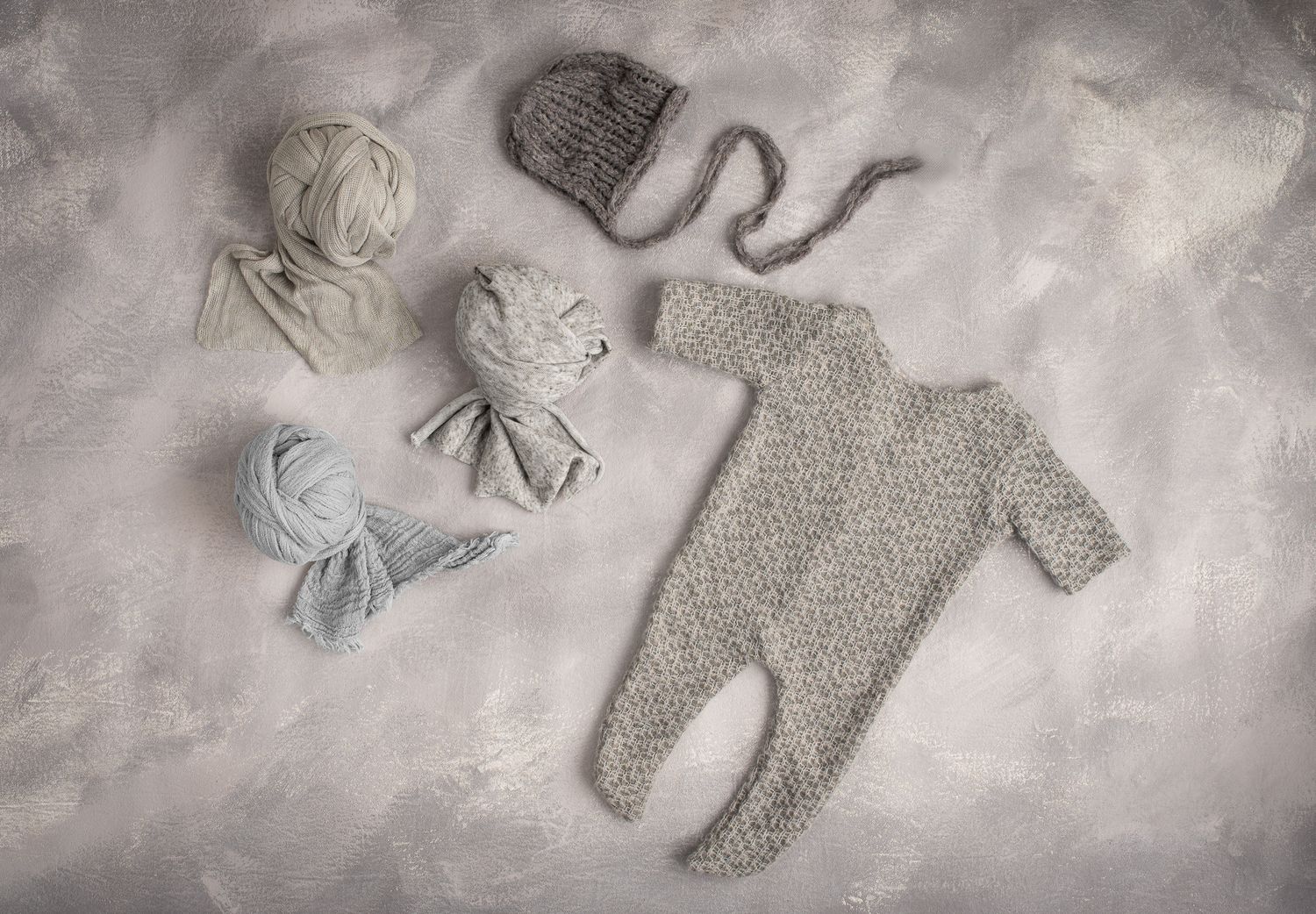 Gray knitted newborn romper with matching hat and gray tones wraps on textured background.