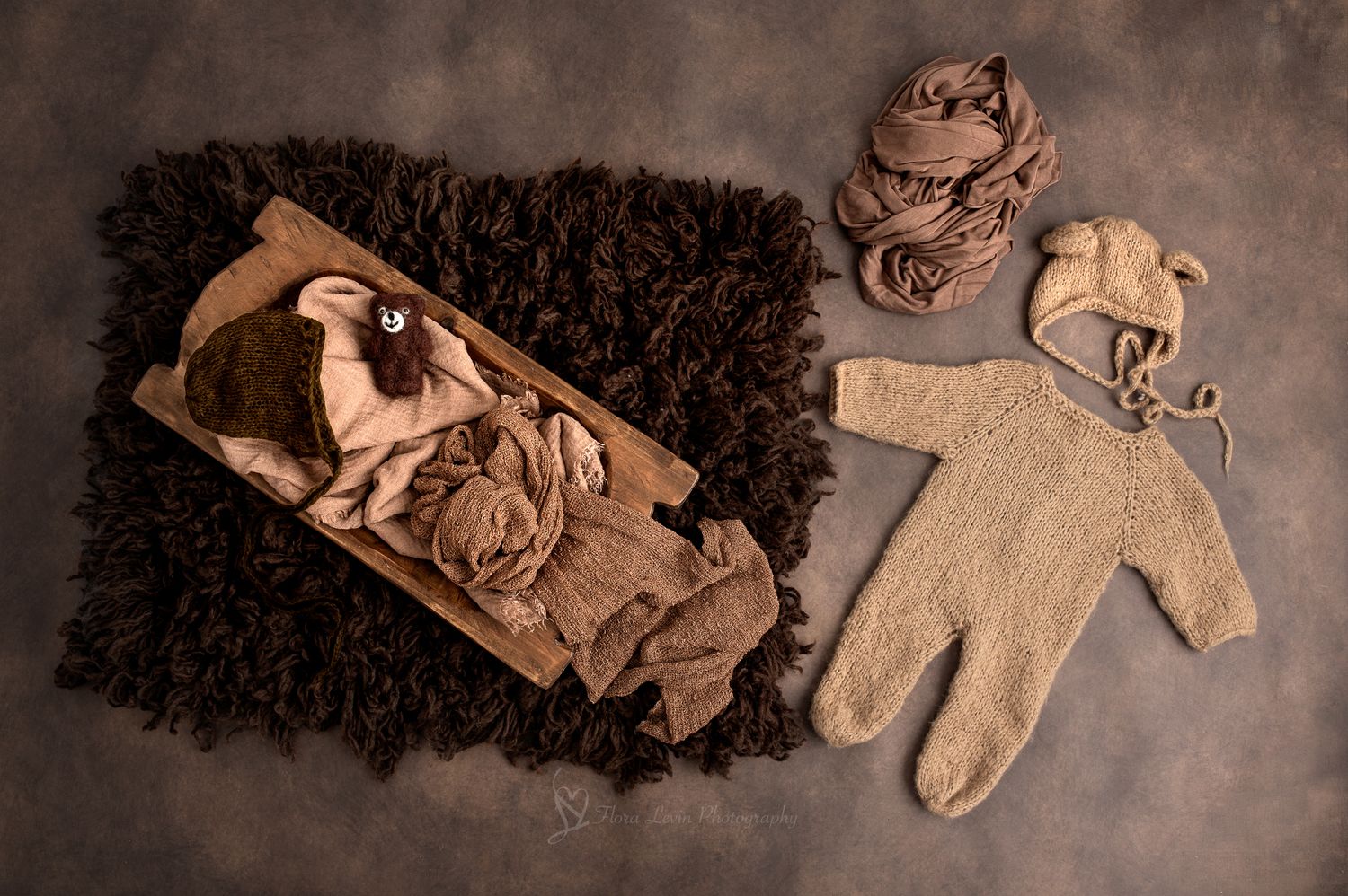 wooden bowl with brown fluffy rug, knit bear bonnet, and beige bear romper outfit nearby.