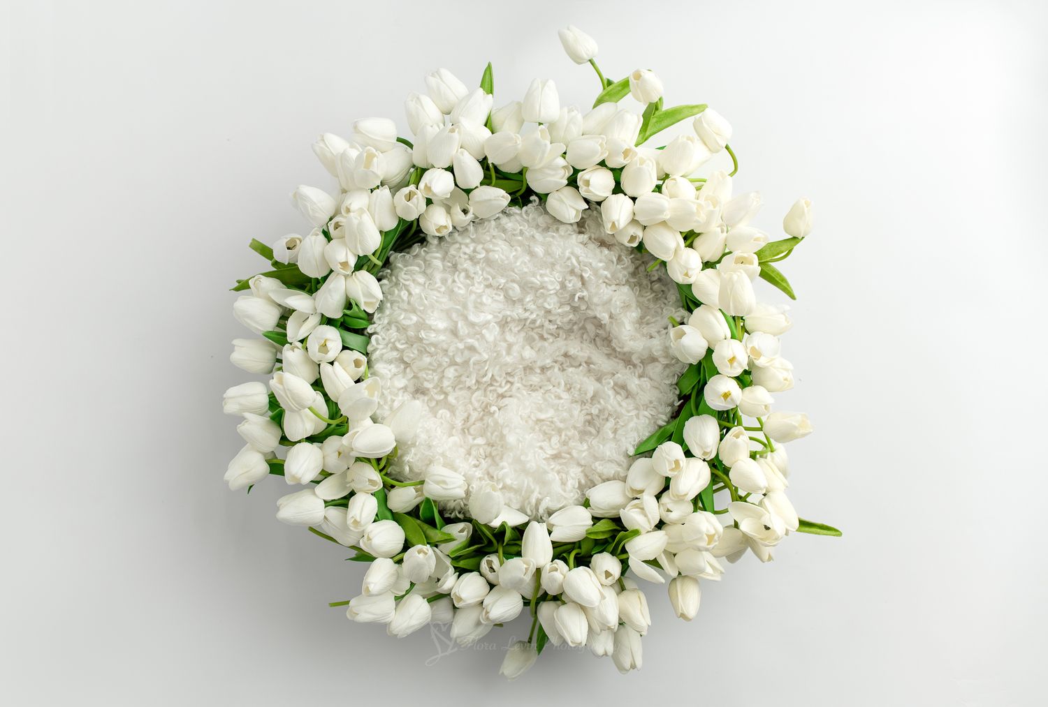 White floral wreath made of tulips and green leaves arranged in a circle filled with white fur.